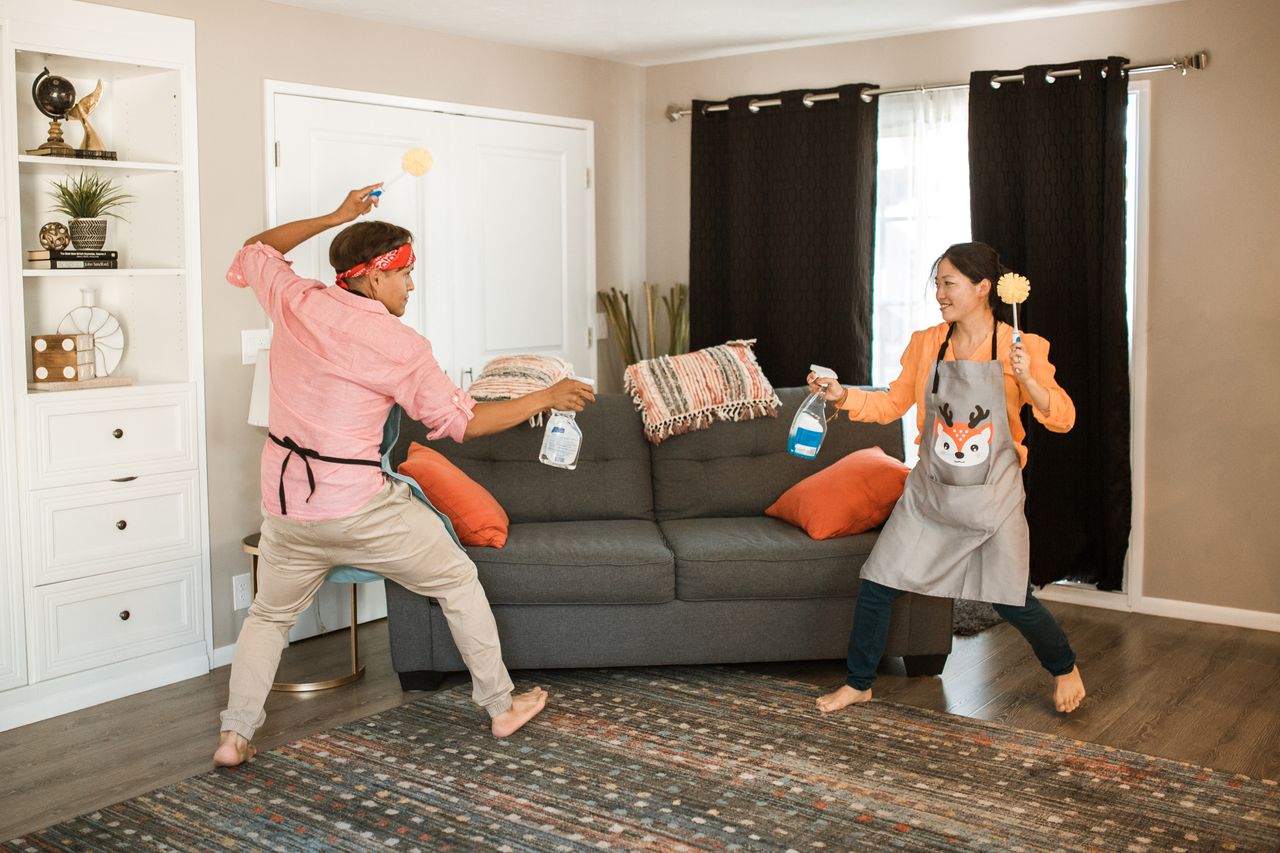 services-03 A joyful couple engages in a playful cleaning fight in their living room, showcasing light-hearted domestic life.